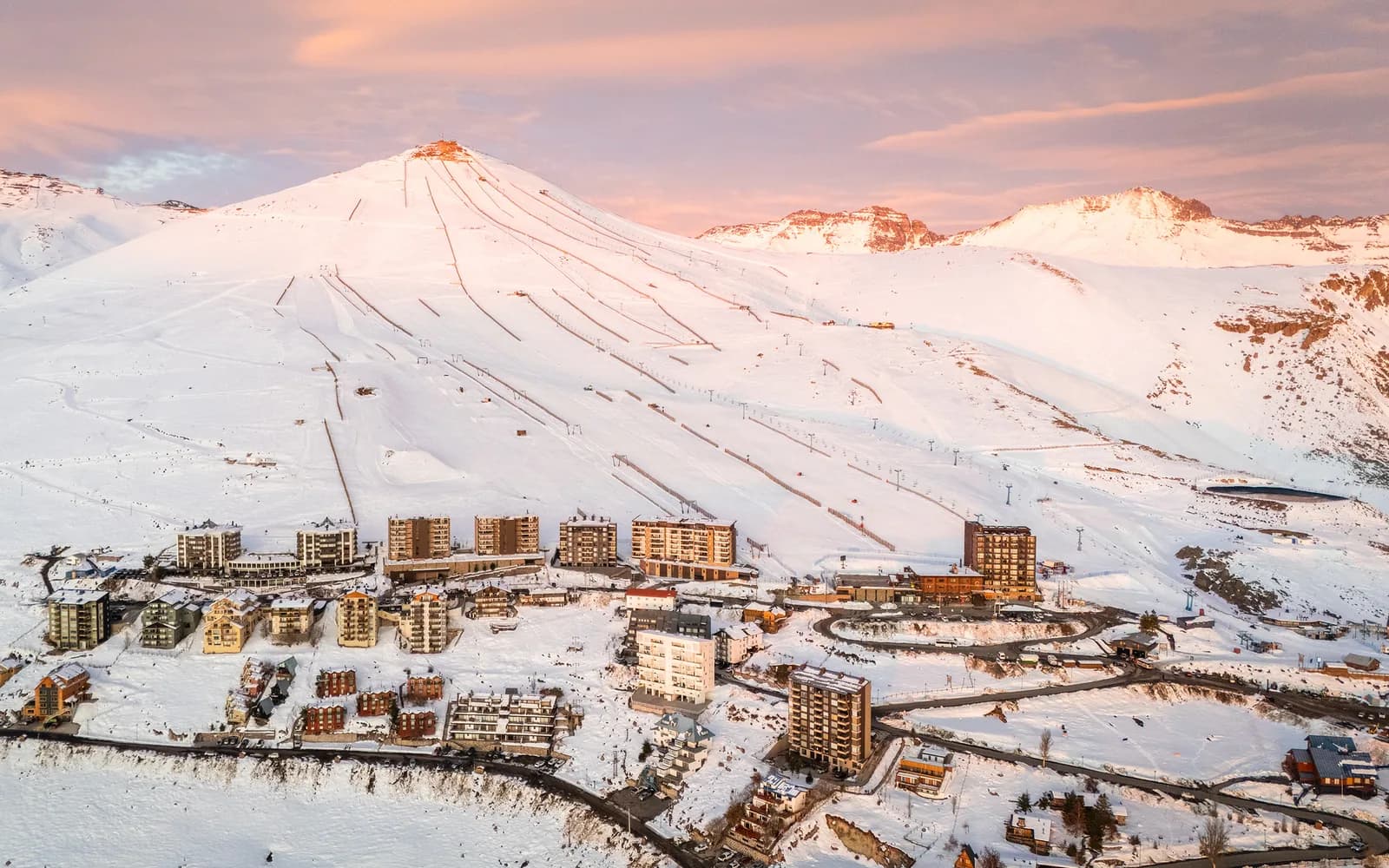 Vista aérea de El Colorado: la ladera nevada con sus pistas y andariveles, y los edificios del centro de esquí al atardecer