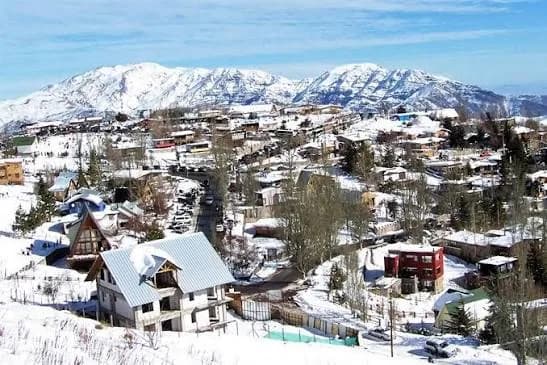 Casas de Farellones cubiertas de nieve, con la cordillera nevada al fondo